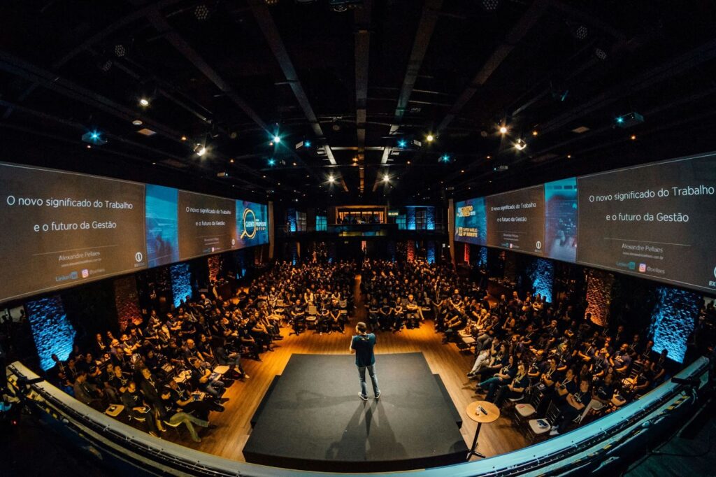 A dynamic shot of a speaker on stage presenting, with a stylized map of Europe projected behind them, highlighting key conference locations.